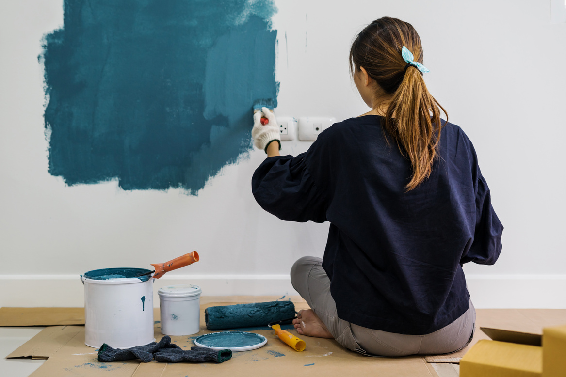 Young asian happy woman painting interior wall with paint roller in new house